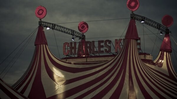 A red and white striped circus big top lit up at night under a dark sky