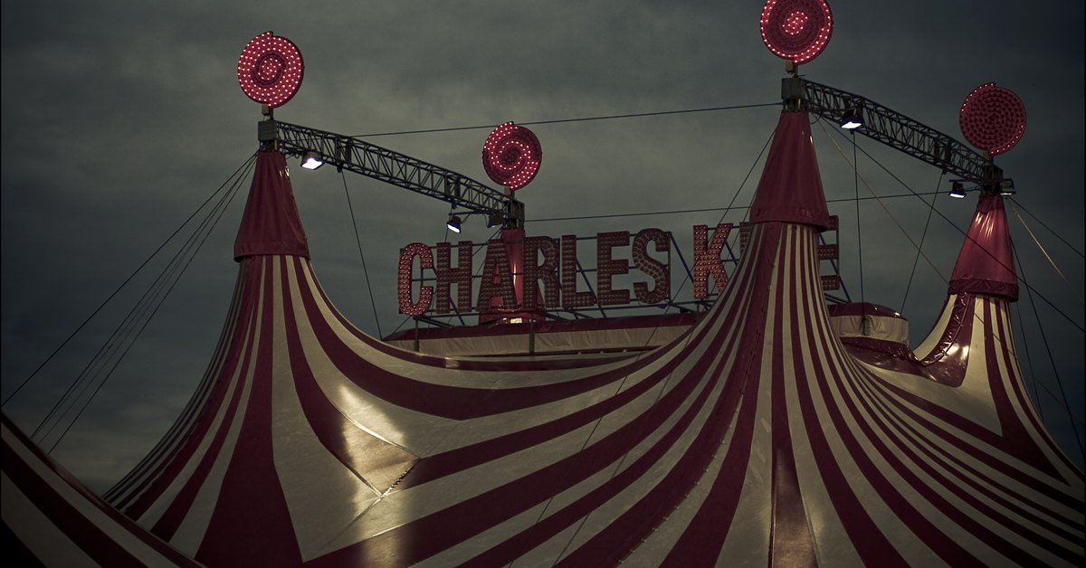 A red and white striped circus big top lit up at night under a dark sky