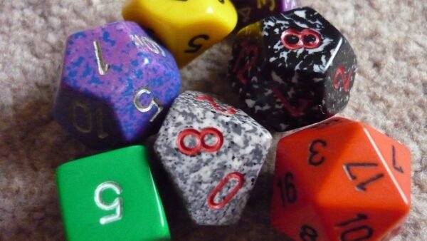 A pile of colorful polyhedral dice, including an orange twenty-sided die, a green six-sided die and a speckled ten-sided die, on a carpet