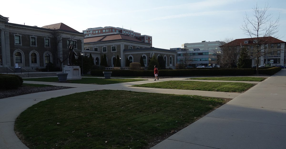 The brick former Nassau County Courthouse in Mineola seen across a lawn and walkways, with a statue near its entrance