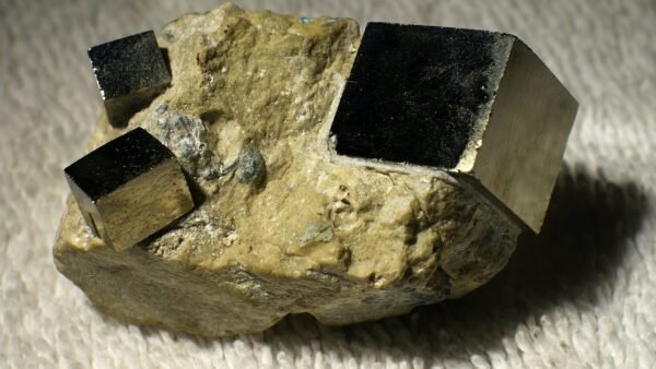 Three shiny, dark metallic cubes of pyrite embedded in a pale lump of rock, resting on a white towel