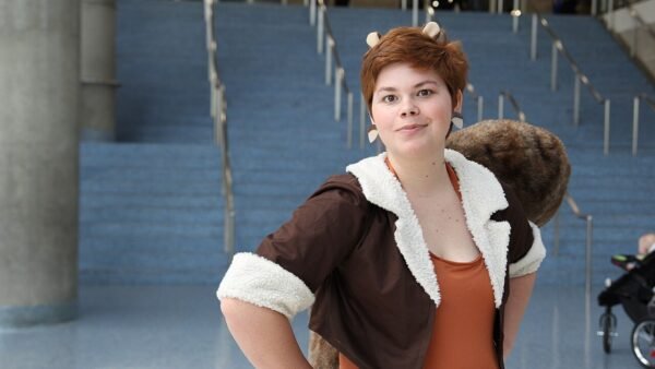 A cosplayer dressed as Squirrel Girl, with squirrel ears, a brown jacket and a bushy tail